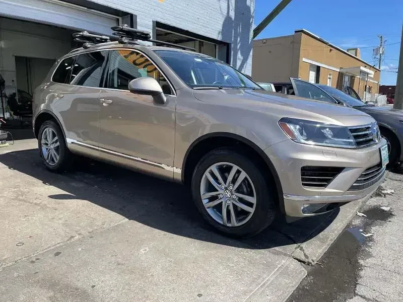A volkswagen touareg is parked on the side of the road in front of a garage.