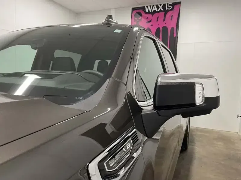 A black truck is parked in front of a sign that says wax is bad.