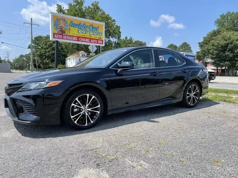 A black toyota camry is parked in a parking lot next to a billboard.