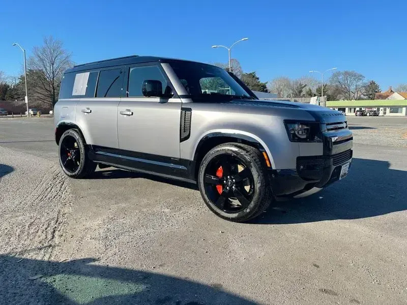 A silver land rover defender is parked in a parking lot.