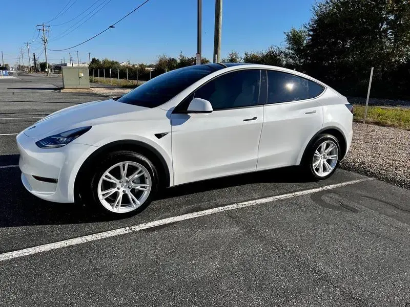A white tesla model y is parked in a parking lot.