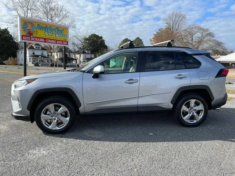 A silver toyota rav4 is parked in front of a car dealership.