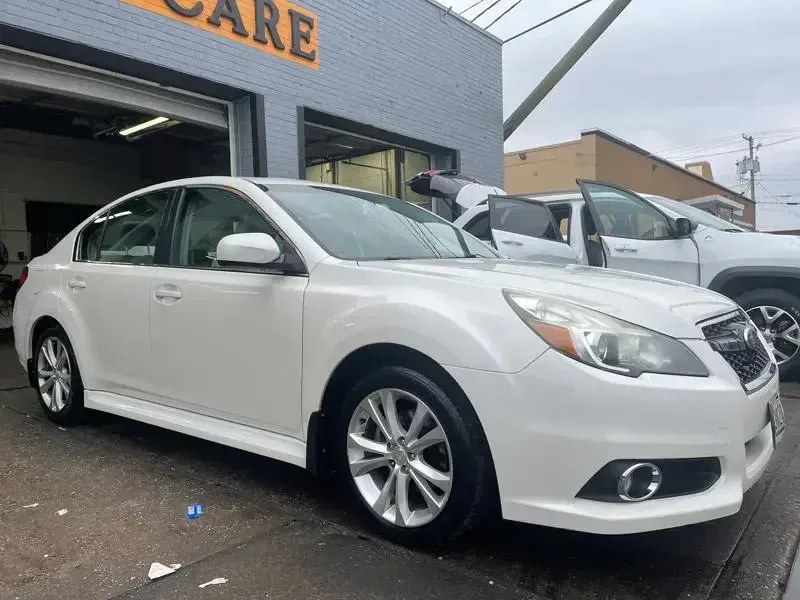 A white car is parked in front of a car dealership.