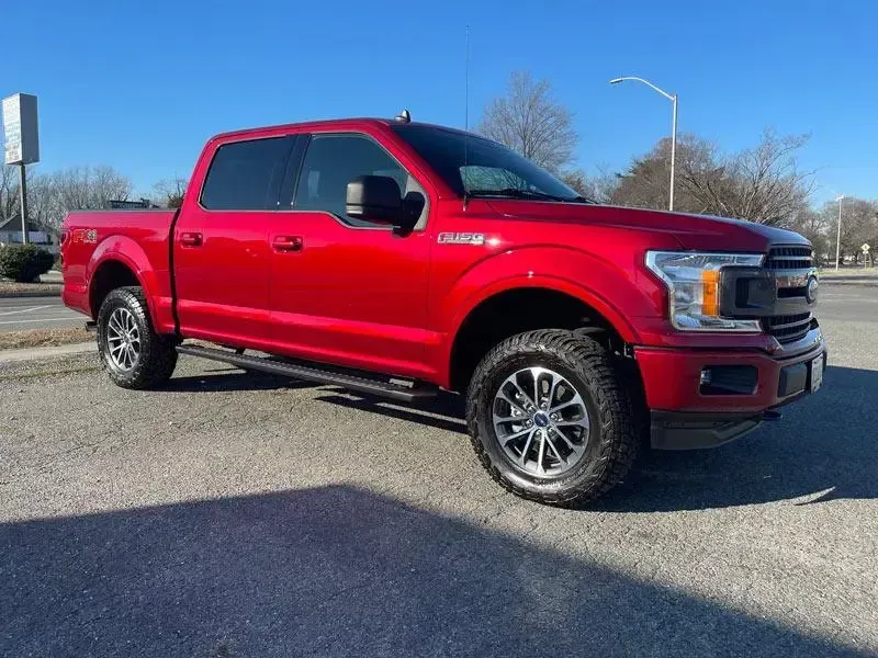 A red ford f150 truck is parked on the side of the road.