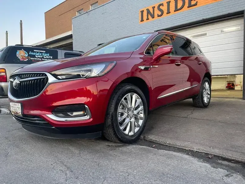 A red buick enclave is parked in front of a garage door.