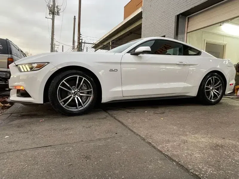A white ford mustang is parked in front of a garage.