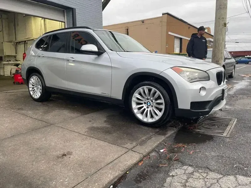 A silver bmw x1 is parked on the side of the road in front of a garage.