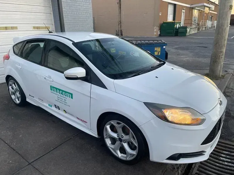 A white ford focus is parked on the side of the road.
