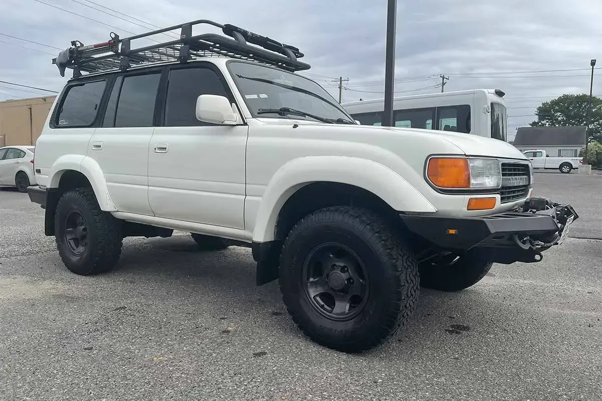 A white toyota land cruiser with a roof rack is parked in a parking lot.