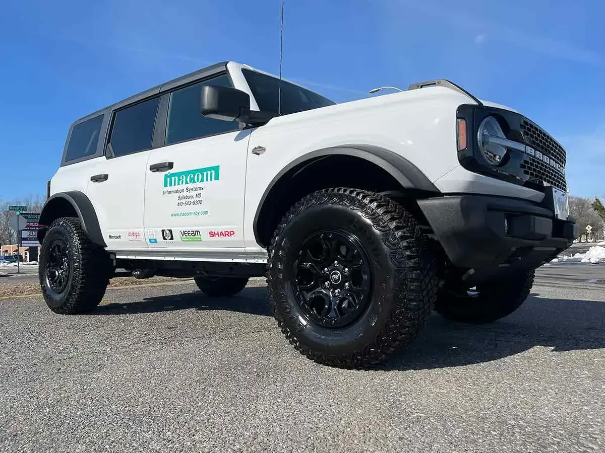 A white ford bronco is parked on a gravel road.