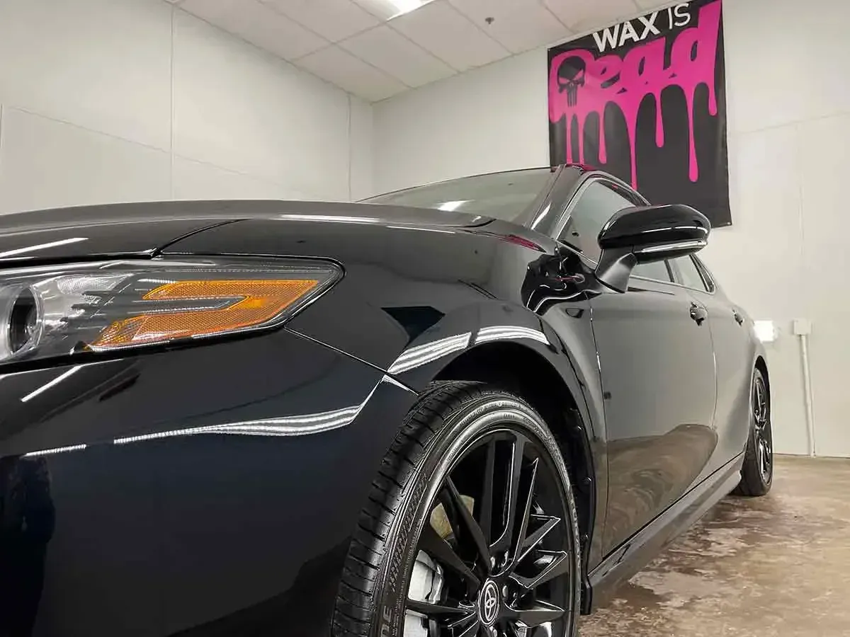 A black car is parked in front of a sign that says wax is.