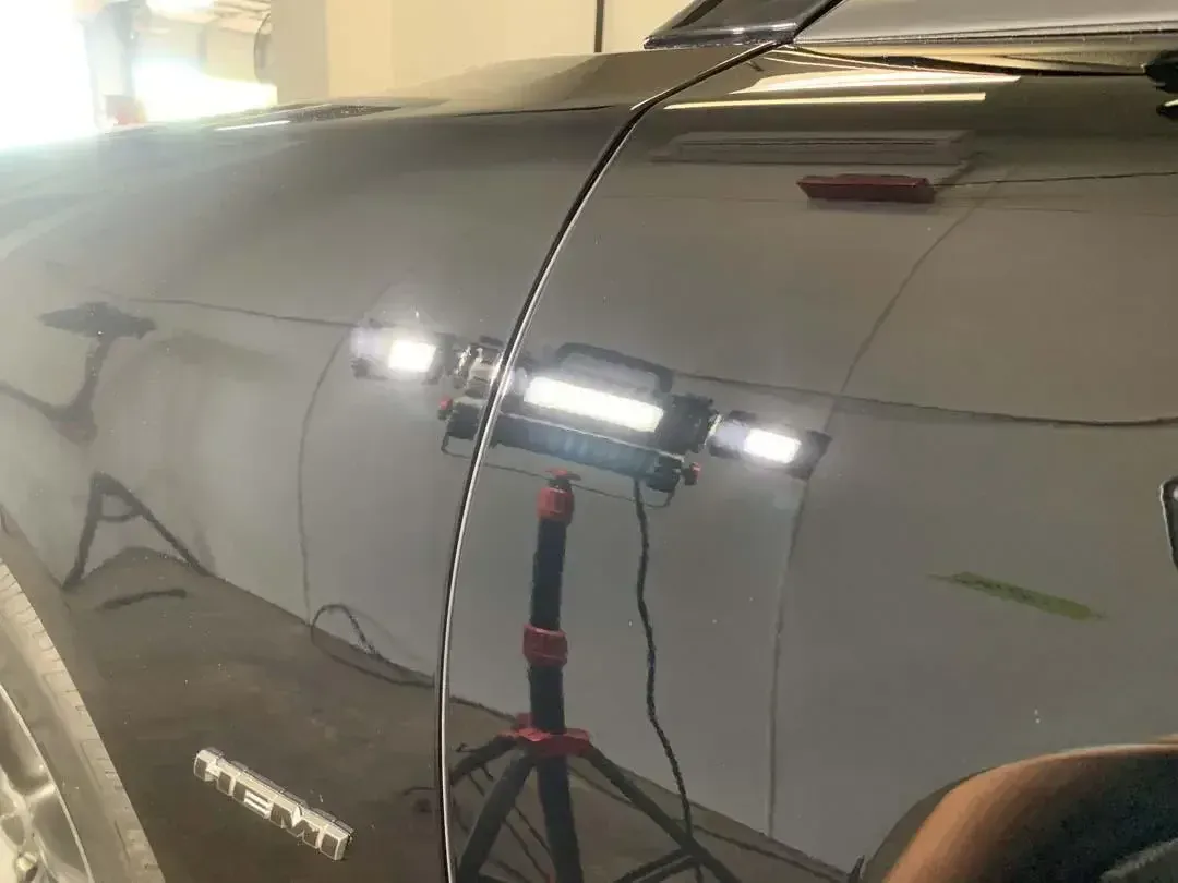 A black car is sitting in a garage with a light on it.