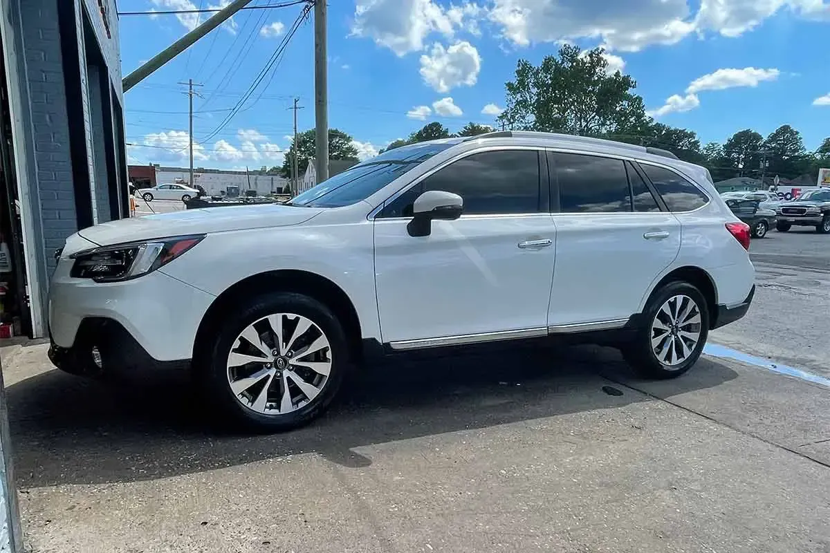 A white subaru outback is parked in a parking lot.