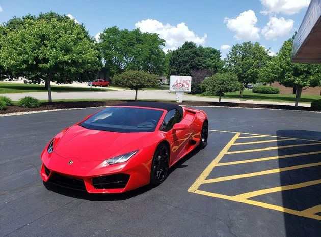 Red Lamborghini convertible parked on asphalt in front of a building on a sunny day.