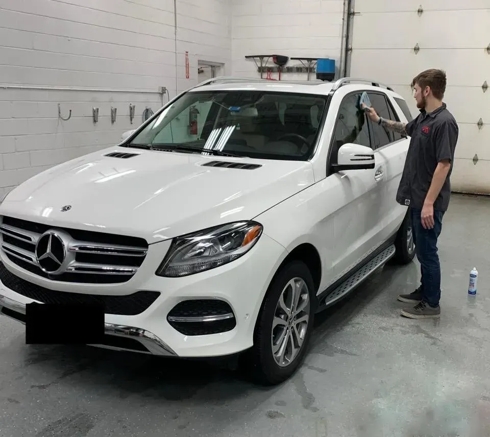 White SUV being worked on by a person in a garage; applying tint to the window.