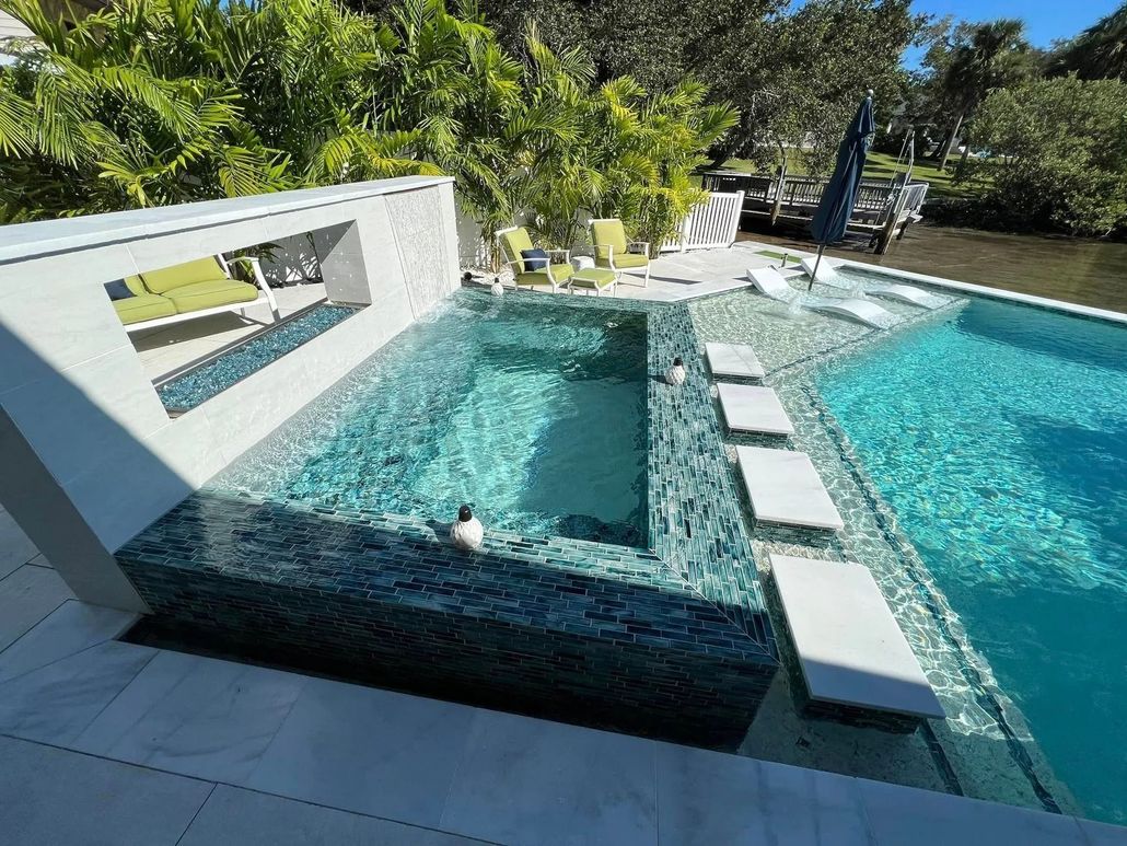 A modern swimming pool with a spa, steps, and water feature, outdoors, blue and white colors.