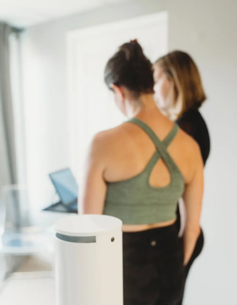 Woman in green sports bra and black pants in front of a laptop, with another woman looking over her shoulder.