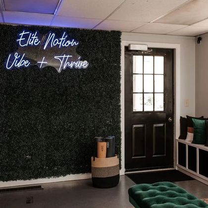 A studio interior with a neon sign on a green wall. Includes a door, seating, and stacked yoga mats.