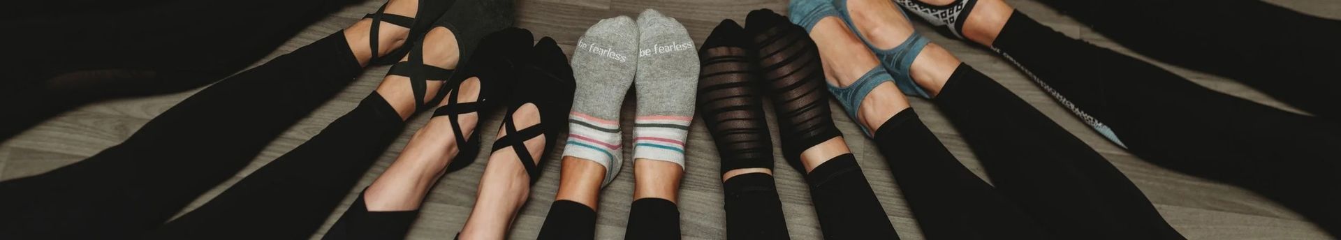 Several pairs of legs and feet wearing various shoes and thigh-high socks on a dark surface.