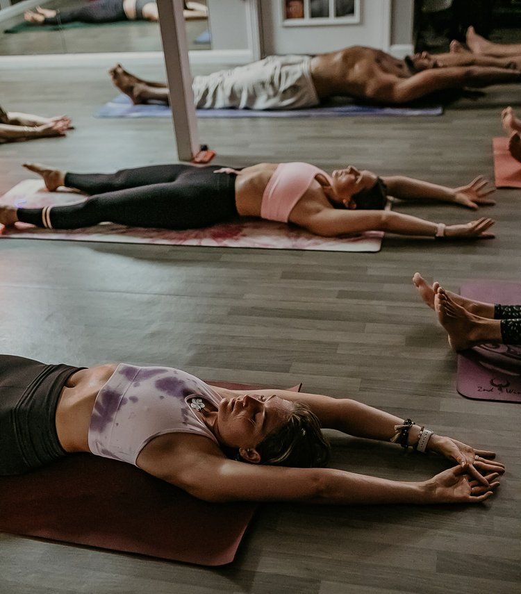 People in a yoga class, lying on mats with arms extended.