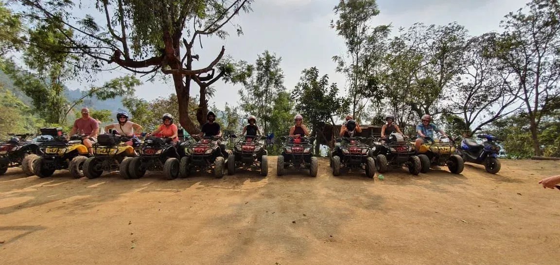 A group of people on ATVs in a dirt area, with trees in the background.