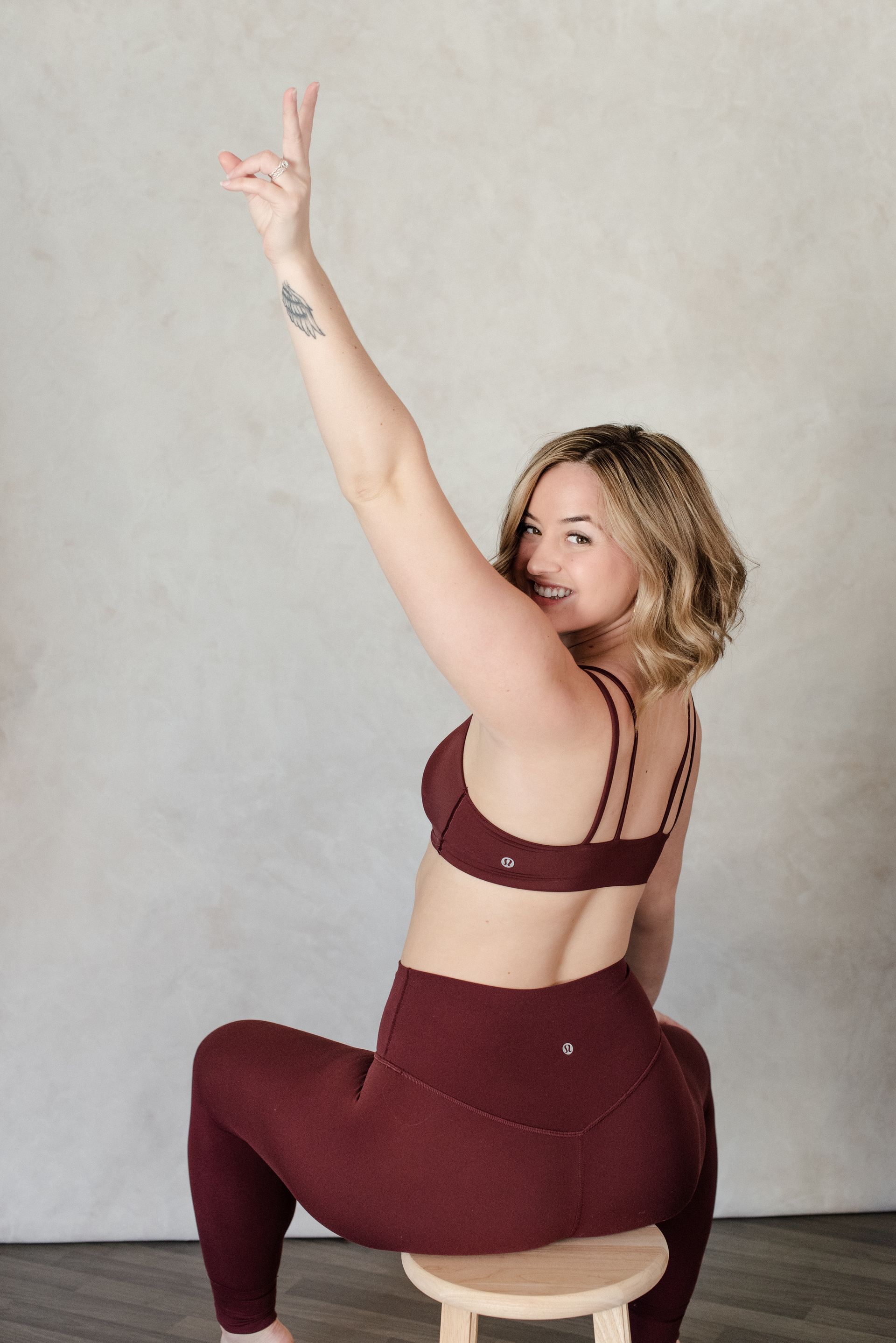 Woman in burgundy workout clothes sitting, raising arm with peace sign.
