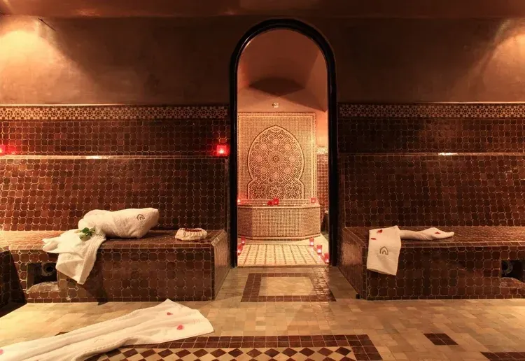 Moroccan bathhouse with tiled walls, arched doorway, benches, and towels.