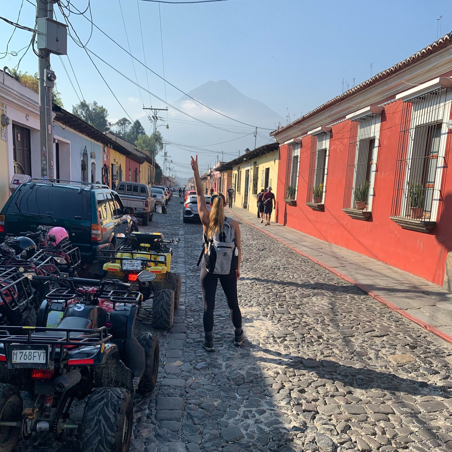 Woman in street with ATV's and volcano in the background. She is giving a peace sign.
