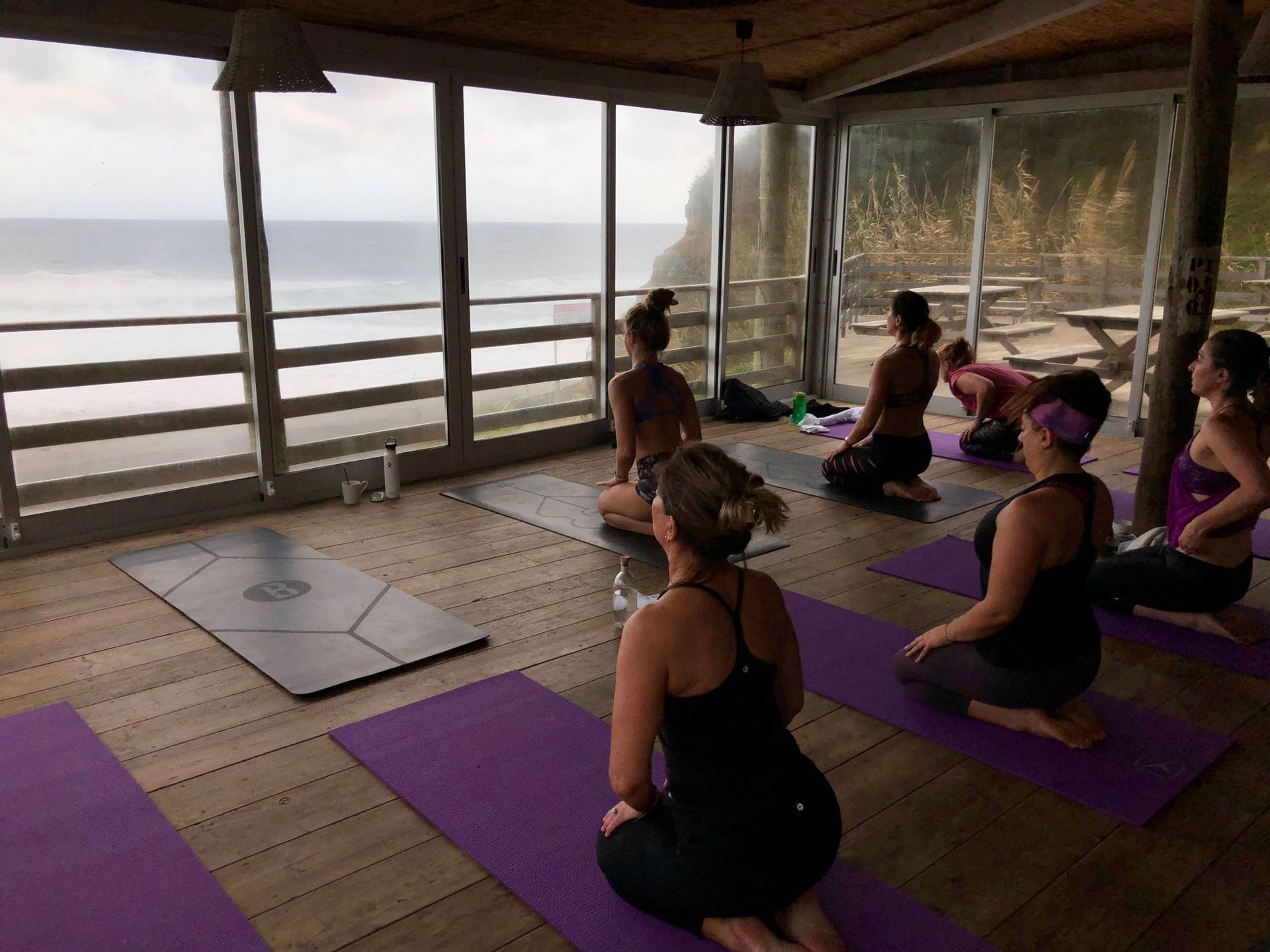 Yoga class overlooking the ocean. People sit on mats, gazing out the window.