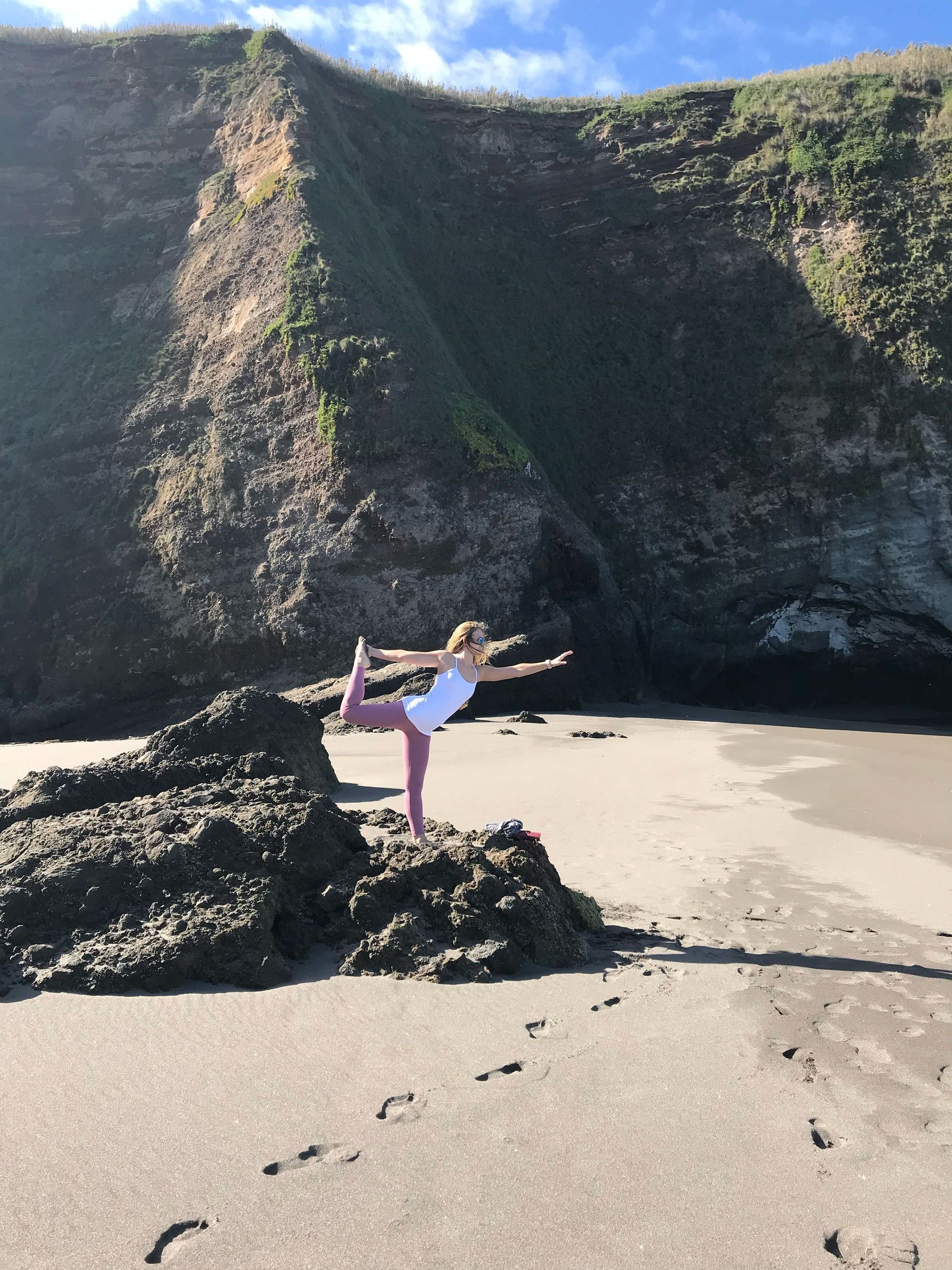 Woman in yoga pose on beach, rocky outcrop, cliff backdrop.