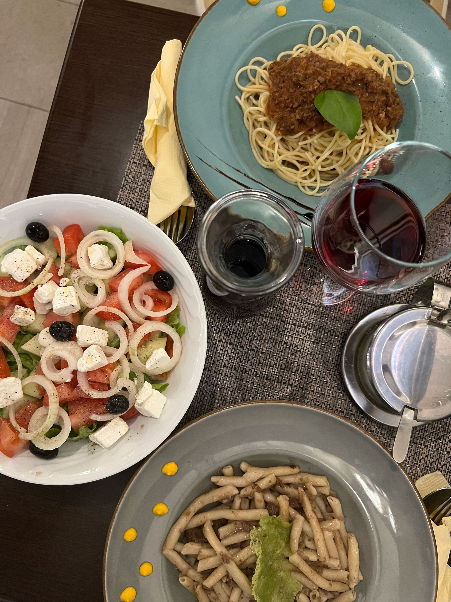 A table set with pasta dishes, Greek salad, wine, and a glass of water.