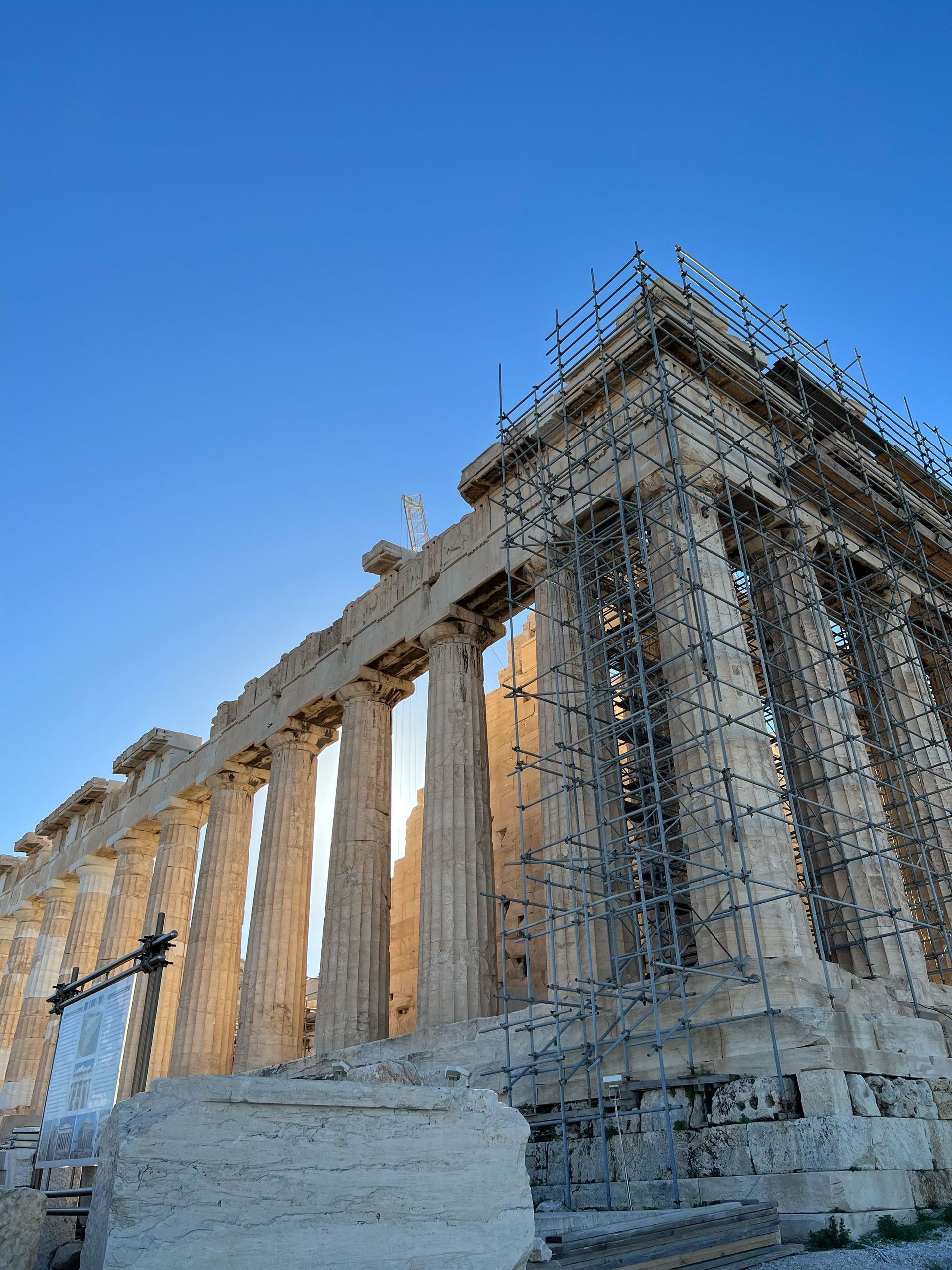 Parthenon temple against a blue sky, under renovation with scaffolding.