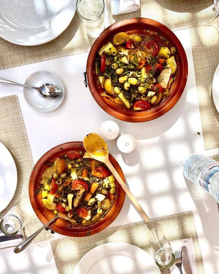 Two tagines filled with stew on a table set for a meal.