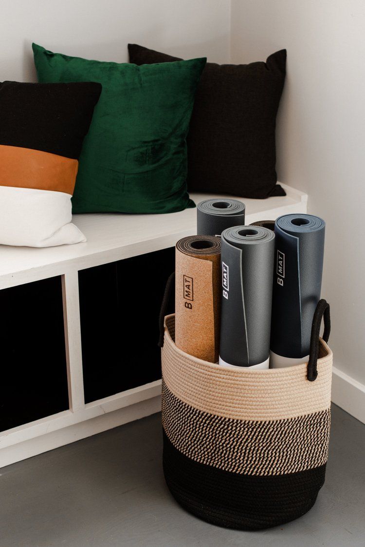 Basket with rolled-up yoga mats and pillows on a white bench.