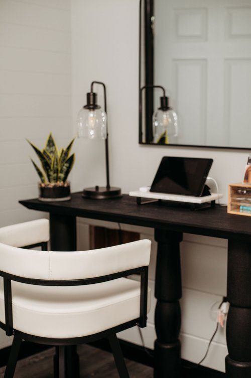 Black desk with white chair, lamp, tablet, mirror, and small plant.