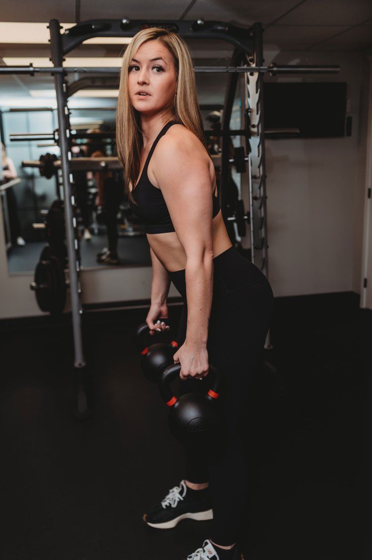 Woman in workout clothes lifting dumbbells in a gym.