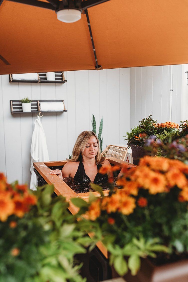 Woman in a tub surrounded by orange flowers under an orange umbrella.