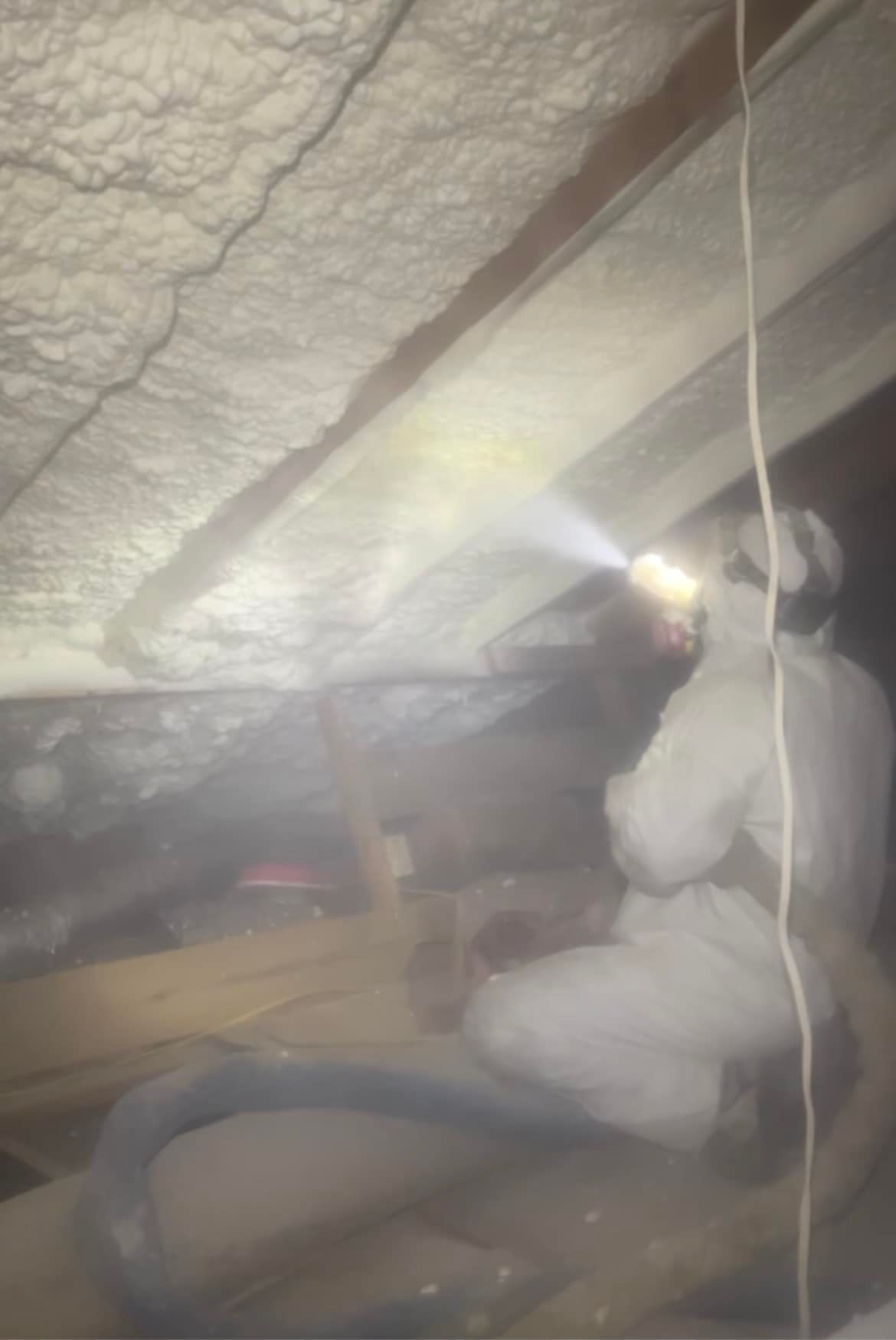 Person in protective suit spraying foam insulation in an attic.