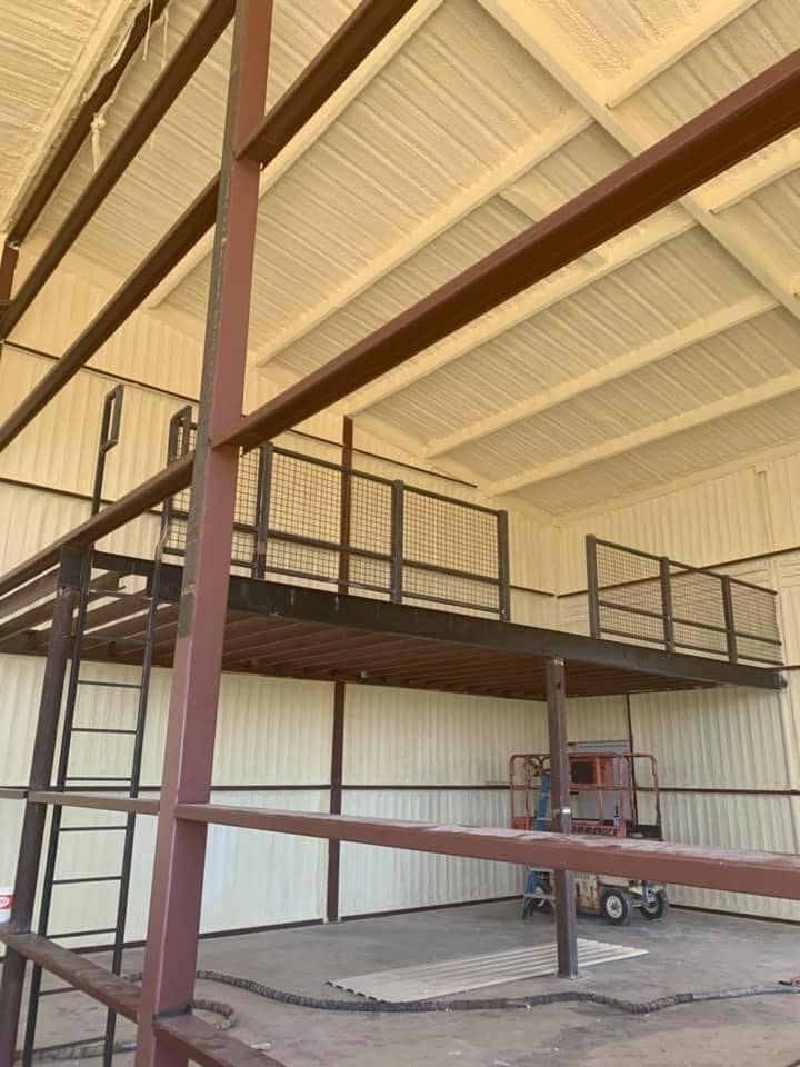Metal structure with a mezzanine, ladder, and a lift inside a building with insulated walls.