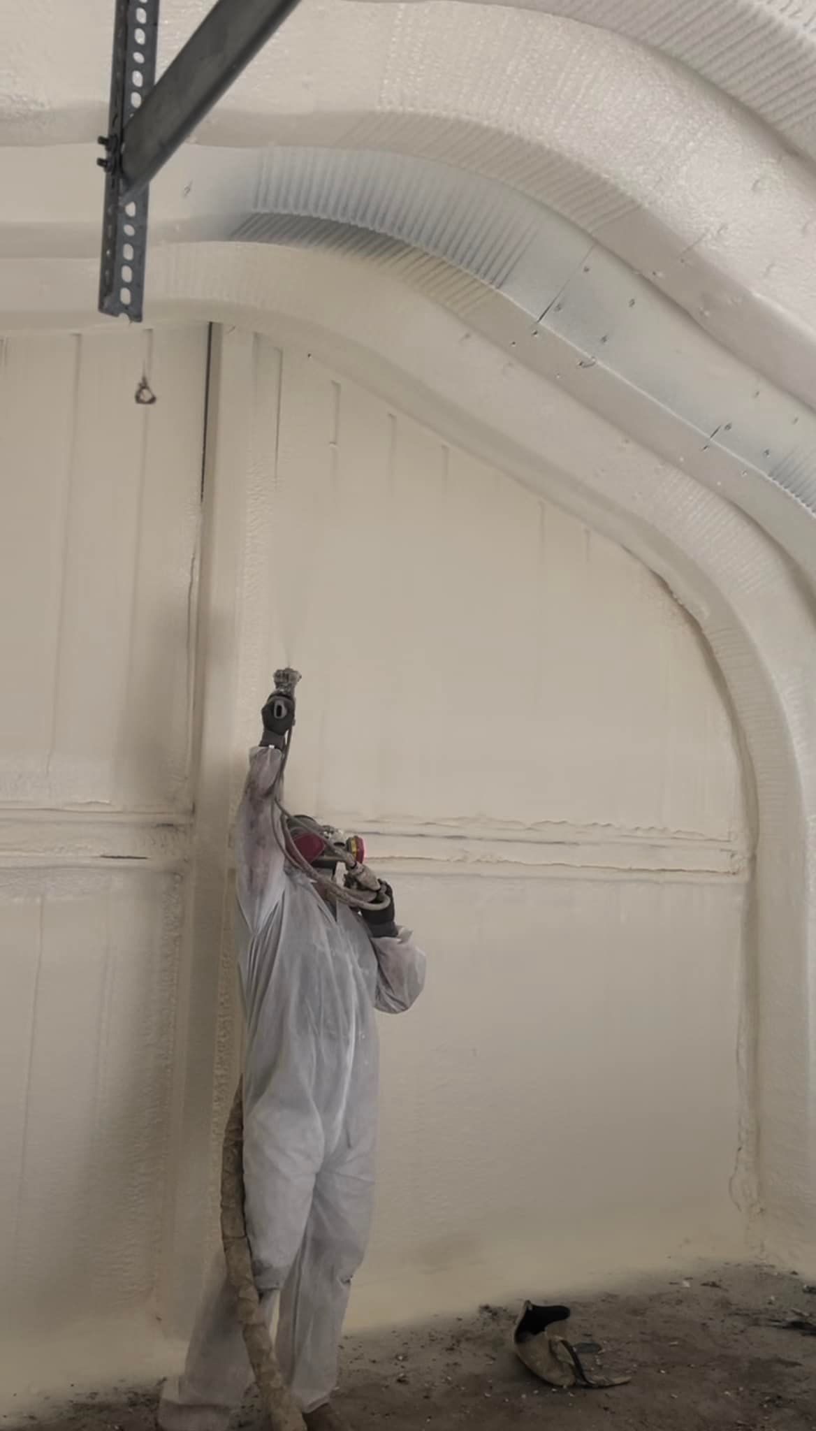 Person spraying insulation on curved wall. Wearing protective suit and mask.