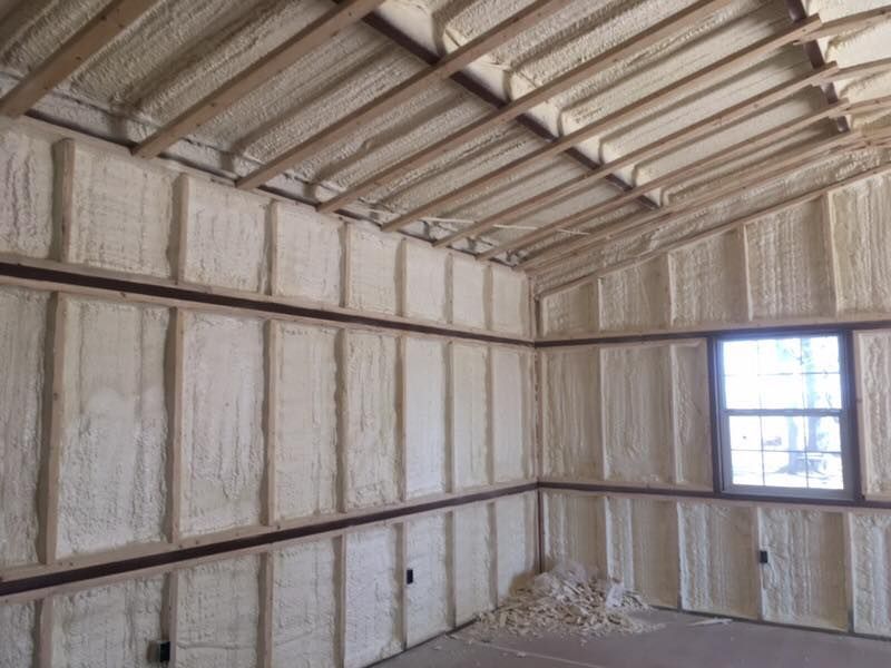 Interior of a building with spray foam insulation on walls and ceiling, brown wooden framing.