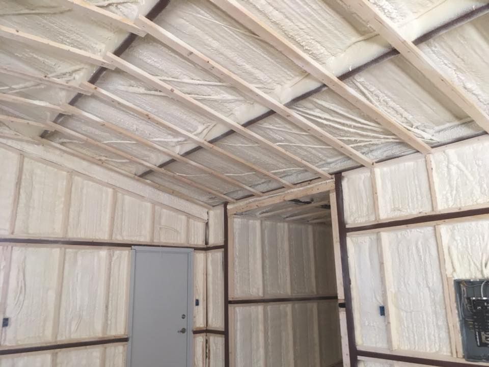 Interior view of a building with spray foam insulation on walls and ceiling, visible wooden beams.