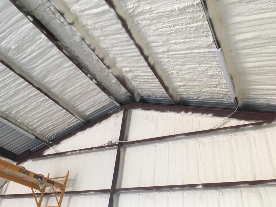 Interior view of a building with spray foam insulation applied to the roof and walls, steel frame visible.