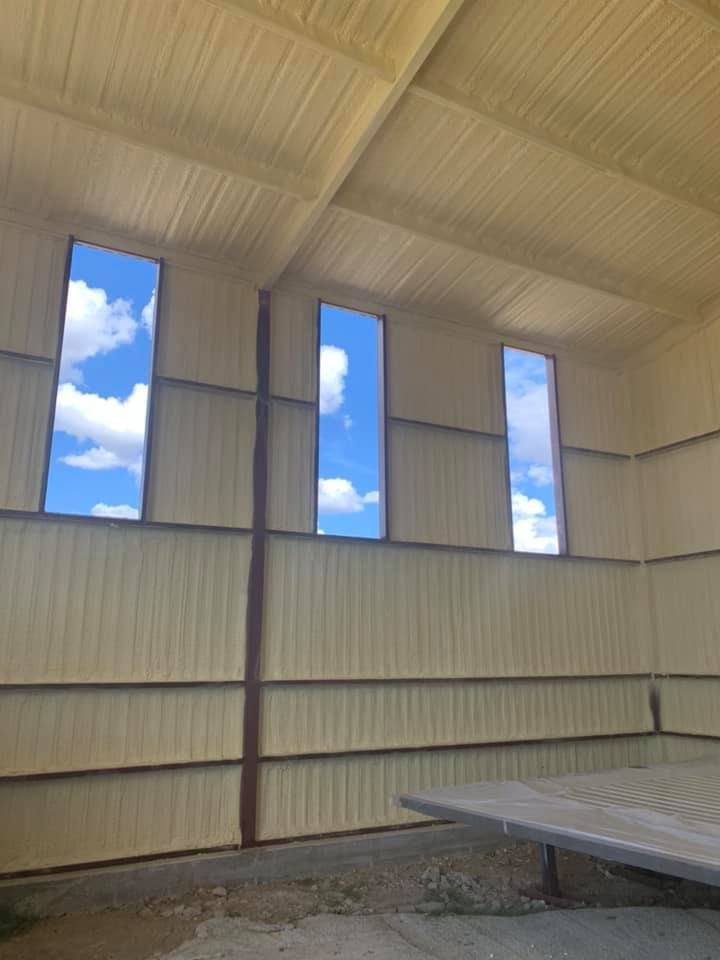 Interior view of a building with spray foam insulation and three narrow windows showing a blue sky with clouds.