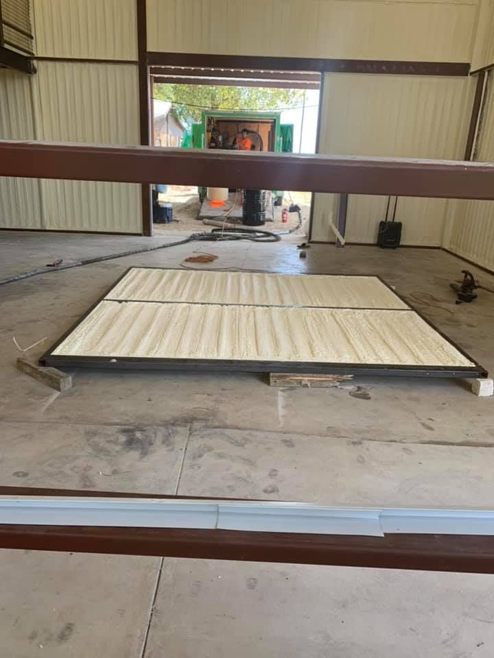 Wooden flooring panels inside a metal building with a large open door at the back.