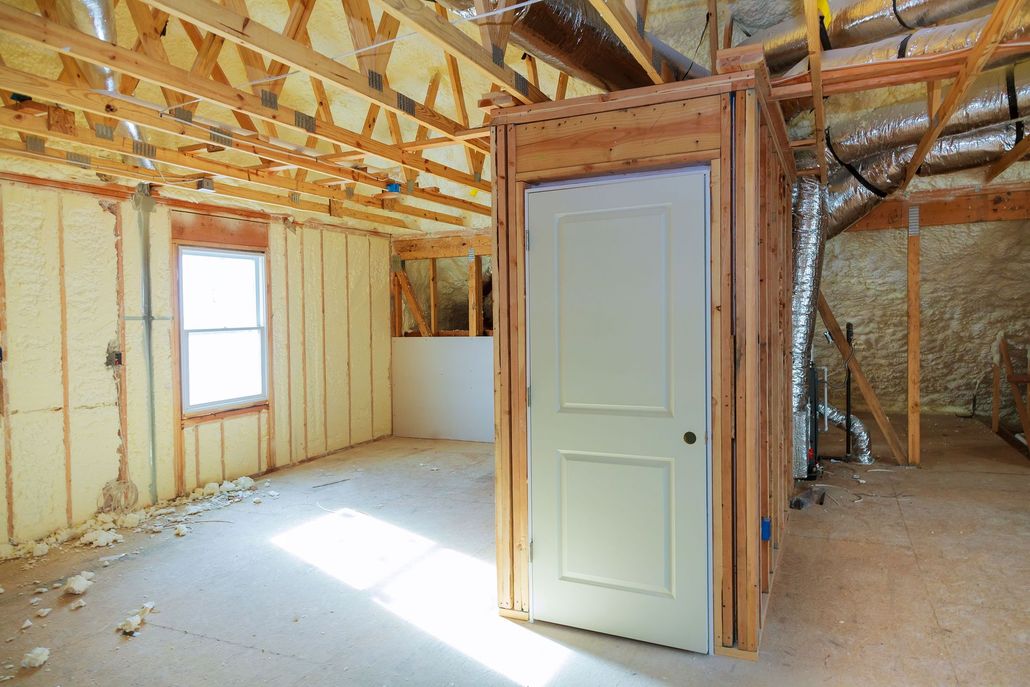 Interior with open wooden beams, spray foam insulation, window, and a white door in a framed structure.