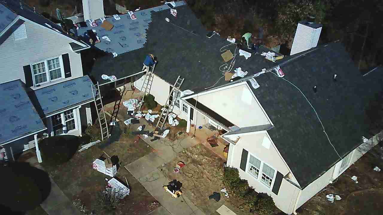 Aerial view of construction workers installing new shingles on a suburban house roof.