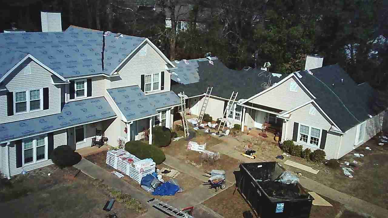 A suburban house with a partially re-roofed top, a dumpster in the yard, and construction materials scattered below.