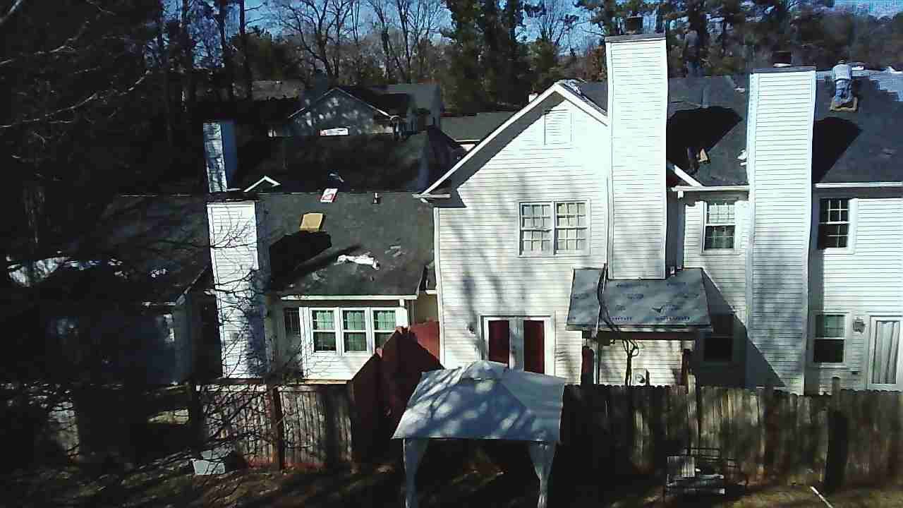 A view of the back of two multi-story white houses with stone chimneys, a small gazebo, and trees in the background.