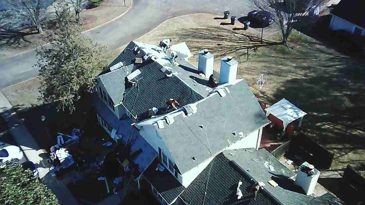 Aerial view of a residential house with a dark shingled roof undergoing construction, featuring several white chimneys.